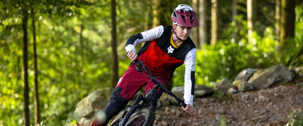 Mountain bike rider in red clothes leaning into a turn on a forest cycle trail