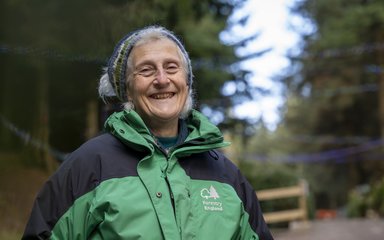 Older woman in Forestry England  jacket smiling in a forest