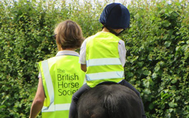 Adult in The British Horse Society high vis walking a child on a horse